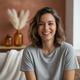 Portrait of a happy young woman with dark hair smiling, wearing a t-shirt in a warm-toned setting.